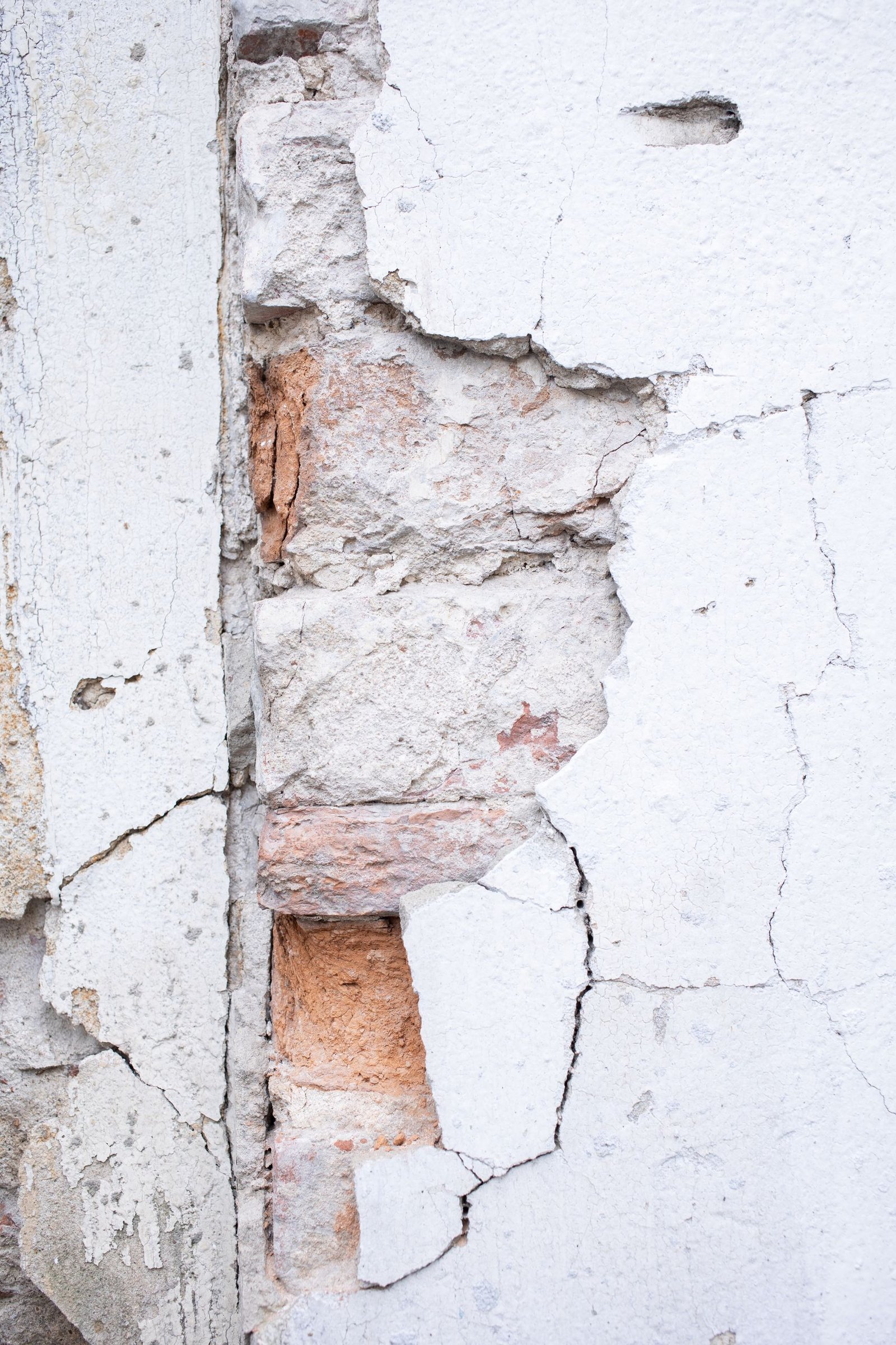 Close-up of a cracked stucco wall revealing bricks underneath. Textured and weathered.